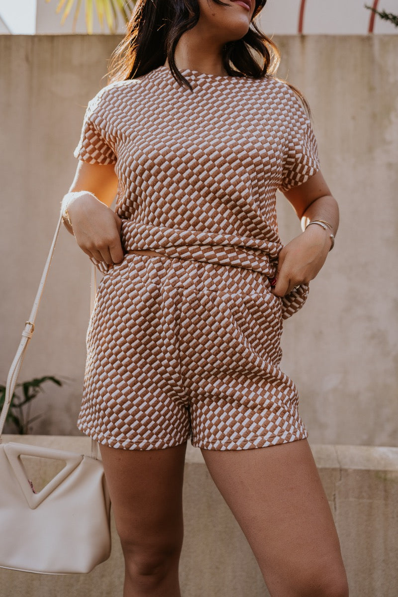 front view of model wearing The Corsica Knit Checkered Shorts features light brown and off white textured knit fabric, skinny checkered pattern, elastic waistband and two side pockets.