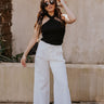 front view of model wearing The Isla White Pleated Pants features white knit fabric, wide pant legs, two side pockets, front zipper with hook closure and belt loops with tie around the waist.