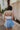 back detail view of model wearing The Azure Denim Ruffle Mini Skirt features washed light blue fabric, shorts lining, mini length, ruffle skirt overlay, flared skirt hem and side zipper closure.