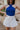 front view of model wearing The Azure White Denim Ruffle Mini Skirt features off white denim fabric, shorts lining, mini length, a ruffled skirt overlay, a flared skirt hem, and a side zipper closure.