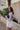 side view of model wearing The Azure White Denim Ruffle Mini Skirt features off white denim fabric, shorts lining, mini length, a ruffled skirt overlay, a flared skirt hem, and a side zipper closure.