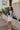 side view of model wearing The Azure White Denim Ruffle Mini Skirt features off white denim fabric, shorts lining, mini length, a ruffled skirt overlay, a flared skirt hem, and a side zipper closure.