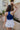 back view of model wearing The Azure White Denim Ruffle Mini Skirt features off white denim fabric, shorts lining, mini length, a ruffled skirt overlay, a flared skirt hem, and a side zipper closure.
