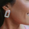 Close up view of model wearing the Naples Village Earring in Pink which features pink round marble bead linked to iridescent rectangle shaped hoop.
