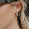 Close up view of model wearing the Summer Glam Earrings which features gold diamond shaped earrings with clear stones.