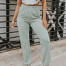 Front view of model wearing the Dreaming On Pants which features light sage fabric, an elastic waistband, and jogger-style legs with elastic ankles.