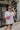 Full body view of model wearing the Travel In Style Sling Bag which features hot pink fabric, adjustable strap with gold hardware and gold zipper closure.