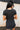 Back view of model wearing the Easy Going Top in Black which features black cotton fabric, a cropped waist, a round neckline, and short sleeves. Top is front tucked.