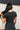 Back view of model wearing the Easy Going Top in Black which features black cotton fabric, a cropped waist, a round neckline, and short sleeves. Top is front tucked.