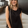 Front view of model wearing the Everything You Love Top in Black which features black satin fabric, a ribbed round neckline, and a sleeveless body with ruffled details.