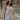 Side view of model wearing the Head In The Clouds Romper which features light grey knit fabric, pockets on each side, a quarter button-up with wooden buttons, a round neckline, and thick straps.