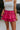Front view of model wearing the Close To You Skort which features hot pink fabric, a skirt overlay with shorts underneath, a mini-length hem, ruffled tiered details, and an elastic/smocked waistband with a tie.