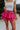 Front view of model wearing the Close To You Skort which features hot pink fabric, a skirt overlay with shorts underneath, a mini-length hem, ruffled tiered details, and an elastic/smocked waistband with a tie.