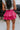 Back view of model wearing the Close To You Skort which features hot pink fabric, a skirt overlay with shorts underneath, a mini-length hem, ruffled tiered details, and an elastic/smocked waistband with a tie.
