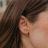 Close up view of model wearing the Cross My Heart Earrings which features gold lines crossed over with clear stones.