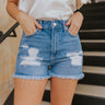 Front view of model wearing the Just USA Denim: Don't Think Twice Shorts which features medium-wash denim fabric, distressed detailing, two front pockets, two back pockets, a frayed hem, a front zipper with button closure, and belt loops on the waistband.