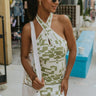 Front view of model wearing the Good Vibes Dress which features cream and green knit fabric with a geometric design, a mini length hem, a halter neckline and an open back.