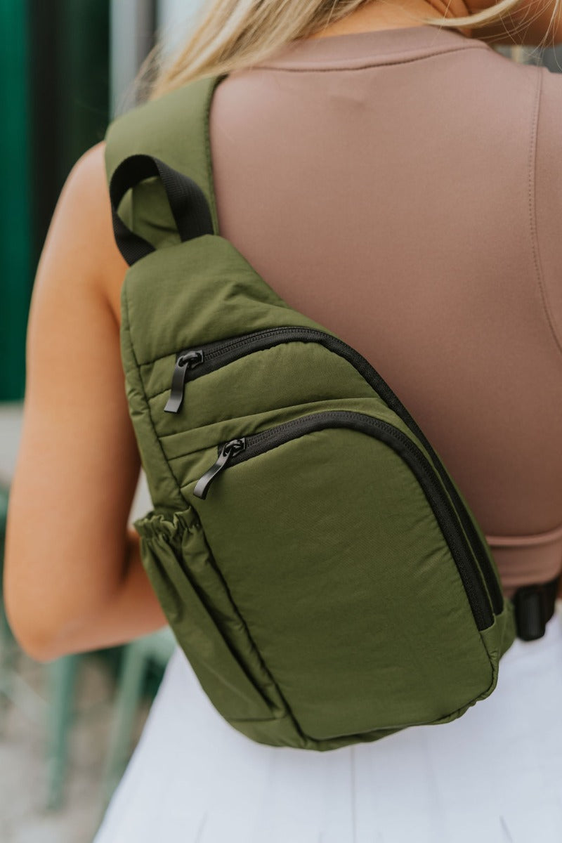 Close up view of model wearing the Long Trip Ahead Sling Bag which features olive fabric, crossbody shoulder style, two front pockets with zipper closure, black hardware and adjustable strap.