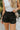 Close front view of model wearing the Making Moves Shorts in Black that have black lightweight fabric, a smocked/elastic high-rise waistband, slits on the side, and black panty lining