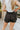 Back view of model wearing the Making Moves Shorts in Black that have black lightweight fabric, a smocked/elastic high-rise waistband, slits on the side, and black panty lining