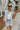 Front view of model wearing the Good For You Denim Vest that has light wash denim fabric, a cropped waist, silver buttons, a collar, front chest pockets, and distressed detailing, light brown stitching.