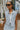 Front view of model wearing the Good For You Denim Vest that has light wash denim fabric, a cropped waist, silver buttons, a collar, front chest pockets, and distressed detailing, light brown stitching.