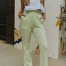 front view of model wearing the For The Record Pants that have soft light green knit fabric, two front pockets, an elastic waistband with drawstring ties, and wide legs.
