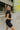 Side view of model wearing the Bring It On Romper that has black stretchy fabric, a romper body, a monochromatic front zipper, a round neckline, and short sleeves.