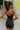 Back view of model wearing the Call It Even Romper that features black stretch fabric, a romper body, a round neckline, bra padding, and adjustable spaghetti straps.