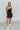 Full body front view of model wearing the Movement Mini Dress in Black that has a ribbed upper body, ribbed shorts lining, a lightweight skirt, a smocked waist, a scoop neck, and thick straps. 