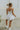 Full body back view of model wearing the Movement Mini Dress in White that has a ribbed upper body, ribbed shorts lining, a lightweight skirt, a smocked waist, a scoop neck, and thick straps