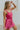 Frontal side view of model wearing the Movement Mini Dress in Pink that has a ribbed upper body, ribbed shorts, a lightweight skirt with a flare out hem, a smocked waist, a scooped neck and thick straps,