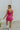 Full body back view of model wearing the Movement Mini Dress in Pink that has a ribbed upper body, ribbed shorts, a lightweight skirt with a flare out hem, a smocked waist, a scooped neck and thick straps,