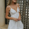 Front view of model wearing the Island Breeze Dress in White that has white fabric with a two-tiered baby doll style, a bubble hem, a plunge neck, adjustable straps, and an open back.