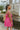 Side view of model wearing the You Have My Heart Dress which features hot pink fabric with a lining, a diagonal ruffle and pleated skirt, a halter neckline that ties around the neck, an open back, and a monochromatic side zipper.