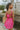 Close up view of model wearing the You Have My Heart Dress which features hot pink fabric with a lining, a diagonal ruffle and pleated skirt, a halter neckline that ties around the neck, an open back, and a monochromatic side zipper.