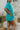 Side view of model wearing the Pool Days Ahead Shorts which features teal textured fabric with a monochromatic checkered print, two front pockets, two back pockets, an elastic waistband and teal lining.