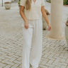 Full body view of model wearing the In Paradise Pants in Ivory which features ivory gauze fabric, an elastic waistband with drawstring ties, and flared legs.