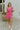 Full body view of model wearing the In the Moment Dress in Pink which features pink sheer fabric with a monochromatic checkered pattern, pink lining, a ruffle hem, a sweetheart neckline with ruffle details, a thick strap and a ruffled short sleeve, and a 