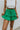 Front view of model wearing the Lucky You Skort which features green fabric with a tiered design, a mini length, green shorts lining, and an elastic waistband with ties.