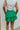 Back view of model wearing the Lucky You Skort which features green fabric with a tiered design, a mini length, green shorts lining, and an elastic waistband with ties.