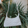 Front view of model holding the Happy Days Purse which features white faux leather fabric, geometric quilted design, gold hardware, zipper closure and shoulder strap.