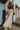 Full body front view of model wearing the Melrose Avenue Pleated Pants that have blush-colored pleated fabric, blush lining, an elastic waistband, and wide legs