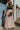 Full body front view of model wearing the Melrose Avenue Pleated Pants that have blush-colored pleated fabric, blush lining, an elastic waistband, and wide legs