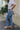 Back view of model wearing the KanCan: Get In Line Jeans that have medium wash denim, a zipper and button closure, front and back pockets, seam details distressed knees, belt loops, and straight legs