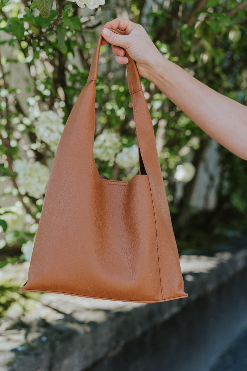 Front view of model holding the Charming Appearance Purse in Mocha which features brown faux leather, snap button closure, 1 inner pocket and shoulder strap.