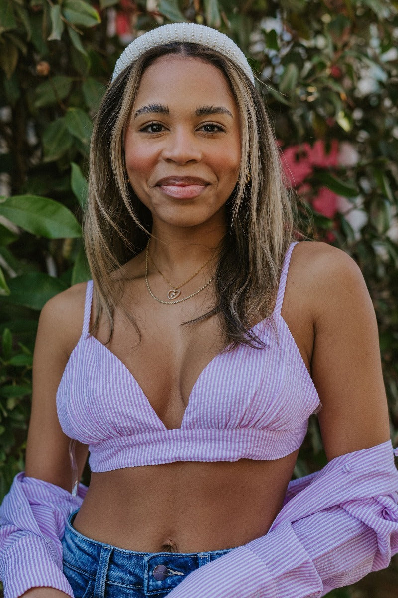 Close front view of model wearing the Laguna Seersucker Bralette in Pink that has a pink and white striped seersucker pattern, adjustable spaghetti straps, and a back tie closure