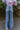 Back view of model sitting while wearing the Rooted Denim: Dallas Flare Jeans that have medium wash denim, a zipper and button closure, front and back pockets, a high-rise waist with belt loops, and flared legs with a distressed hem