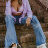 Front view of model sitting while wearing the Rooted Denim: Dallas Flare Jeans that have medium wash denim, a zipper and button closure, front and back pockets, a high-rise waist with belt loops, and flared legs with a distressed hem