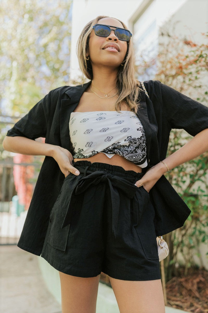 Front view of model wearing the Modern Romance Shorts which features black fabric, a high-rise elastic waistband, a tie around the waistline, two front pockets, and black shorts lining.